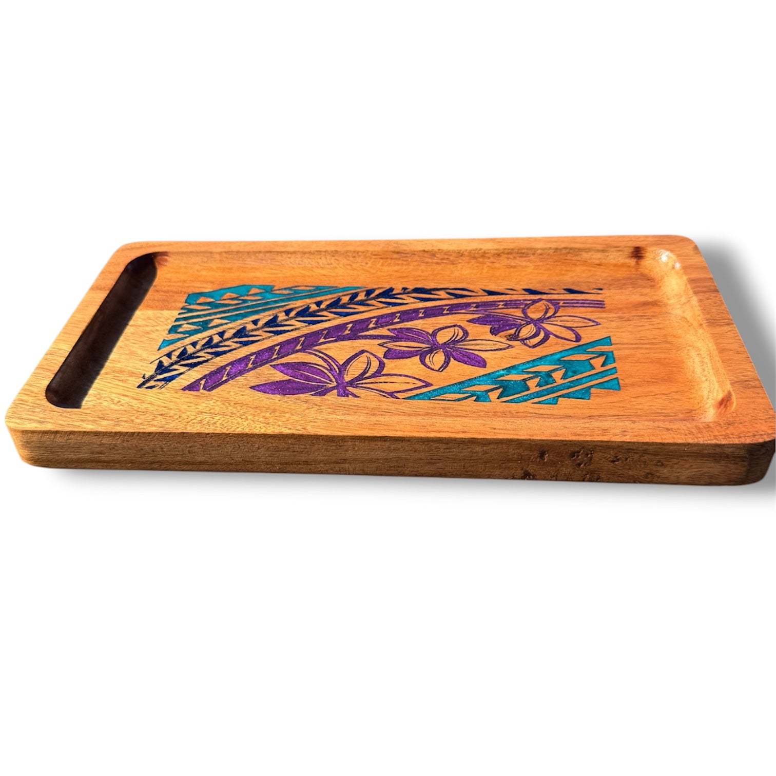 A rectangular wooden serving tray with a handle cutout on one side, featuring a Polynesian-style geometric and floral design in purple and teal on a light brown wood surface, shown on a white background.