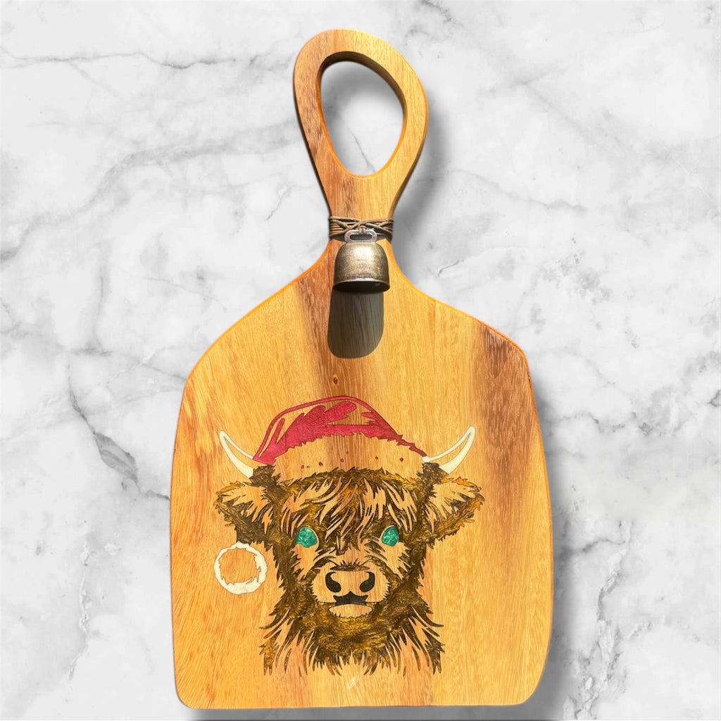 Wooden paddle with a highland cow design and bell on a marble background