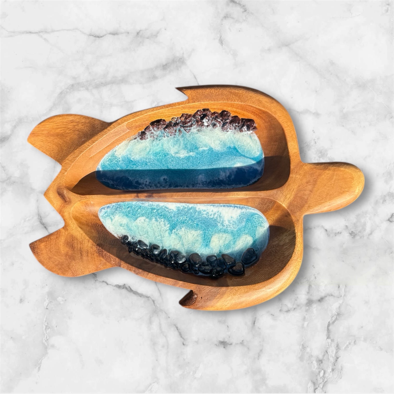 Wooden fish-shaped platter with blue resin and black stone design on a marble background